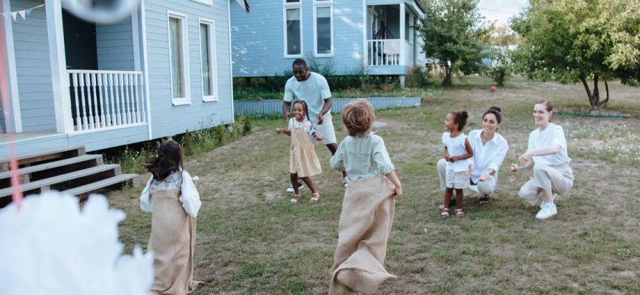 Children and adults have fun with a lively sack race outside a cozy home on a sunny day.
