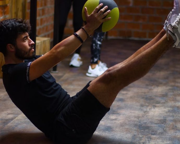 Focused man performing core exercises with a medicine ball in an indoor gym highlighting fitness and strength.