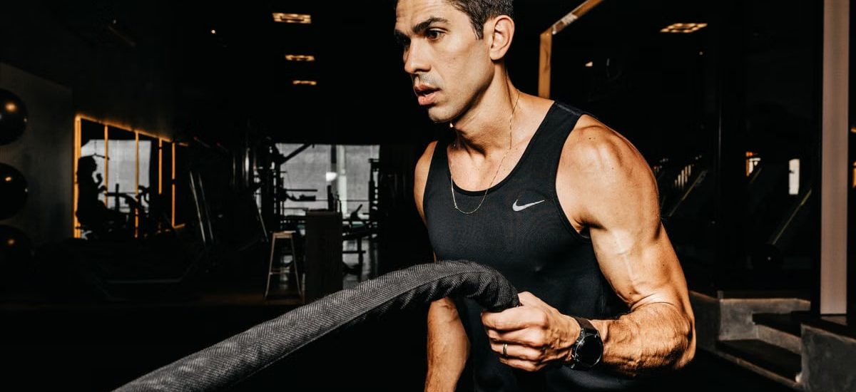 A determined male athlete working out with battle ropes in a dimly lit gym, showcasing strength and fitness.